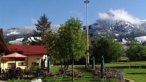 A rural setting with a building that has a red roof, a tall street lamp, and a mountain backdrop with snow. - Wiesengrund (Bad Hindelang)