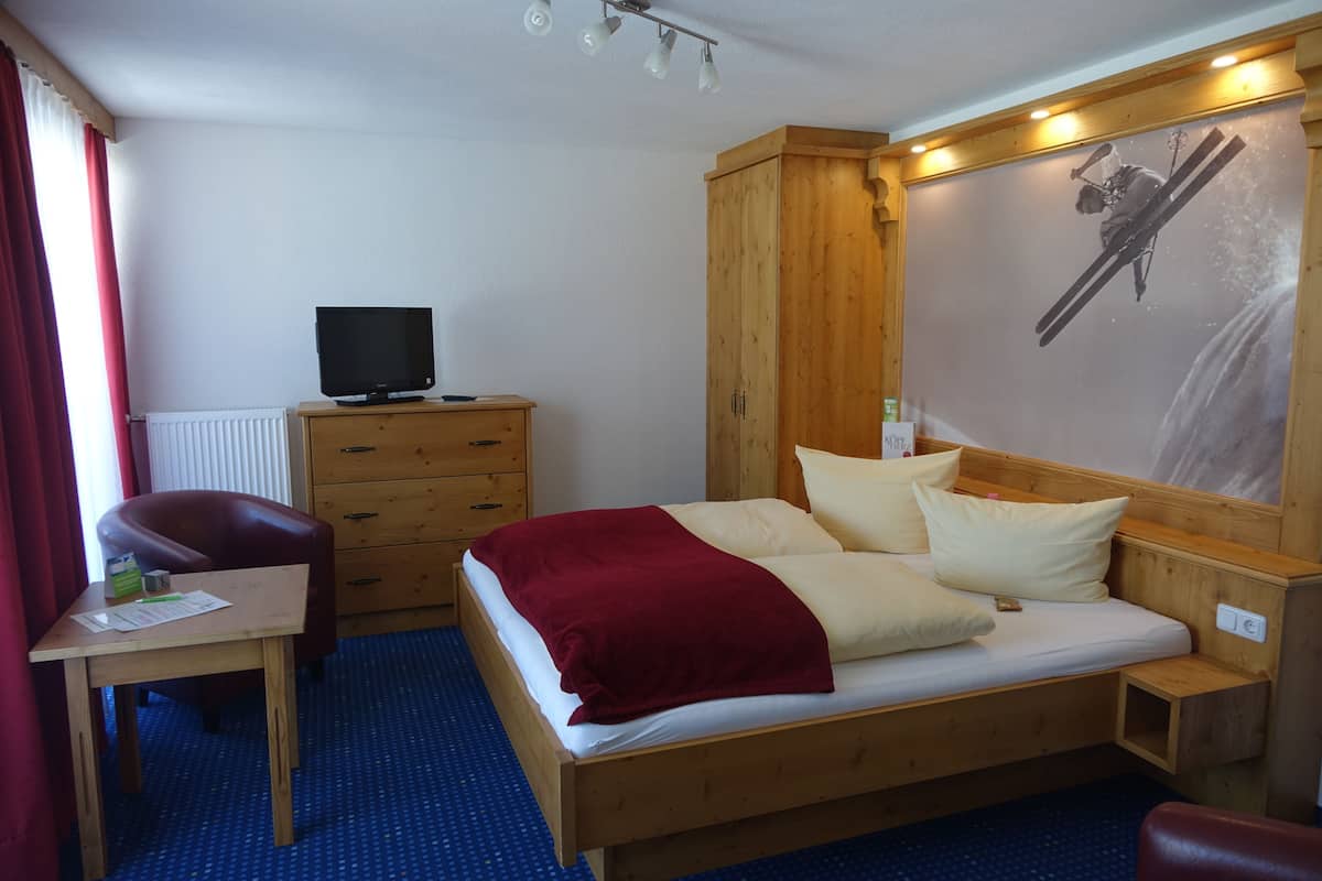 A hotel room with a wooden bed, a desk with a computer, a television, and a ski-themed wall mural.