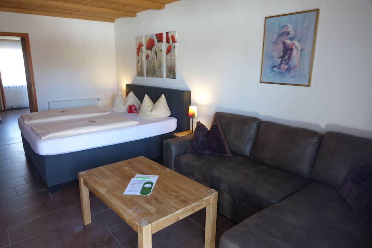 A bedroom with a bed, a wooden table, a sofa, and a painting on the wall.