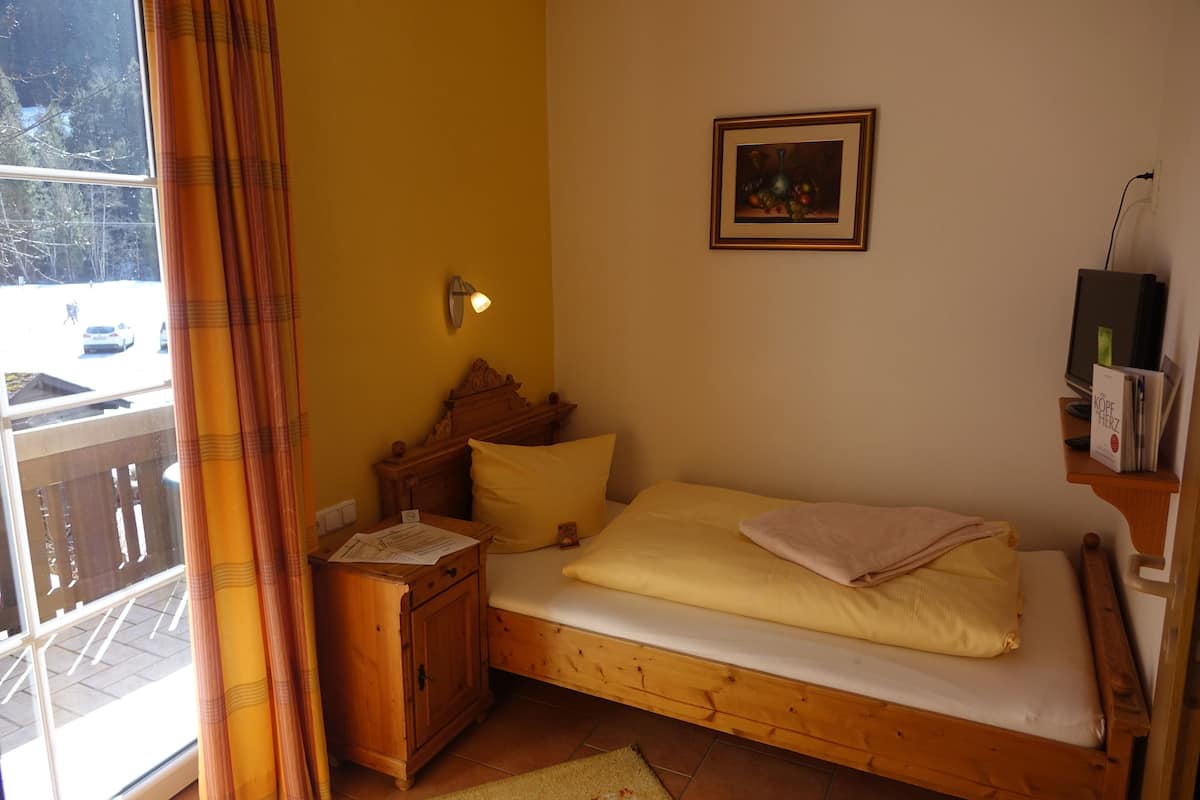 A small, cozy bedroom with a wooden bed, a nightstand, a wall-mounted lamp, and a framed picture.