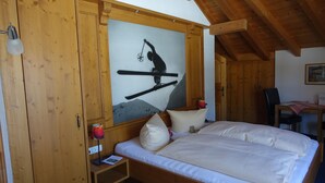 A wooden room with a bed, a painting of a skier, and a desk with a chair. - Wiesengrund (Bad Hindelang)