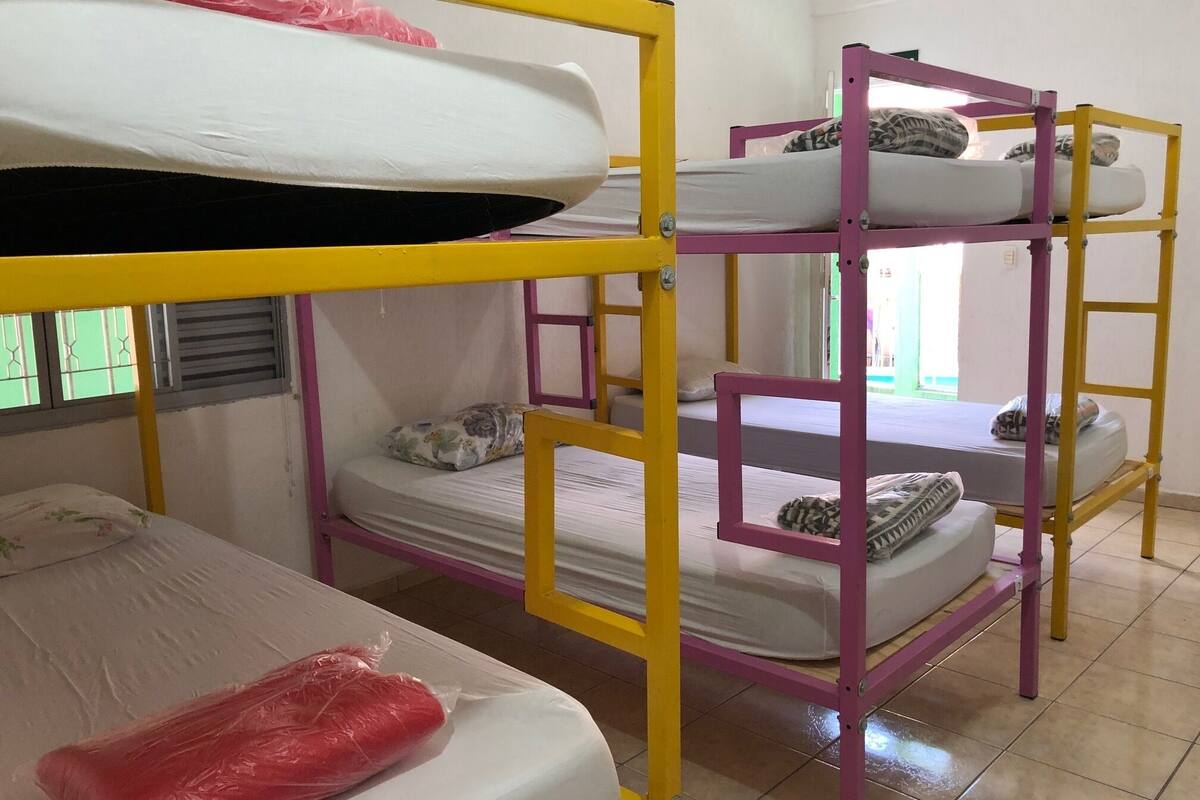 Habitación con literas, barandillas amarillas y rosas, un colchón en la litera inferior y una bolsa de plástico sobre la cama.