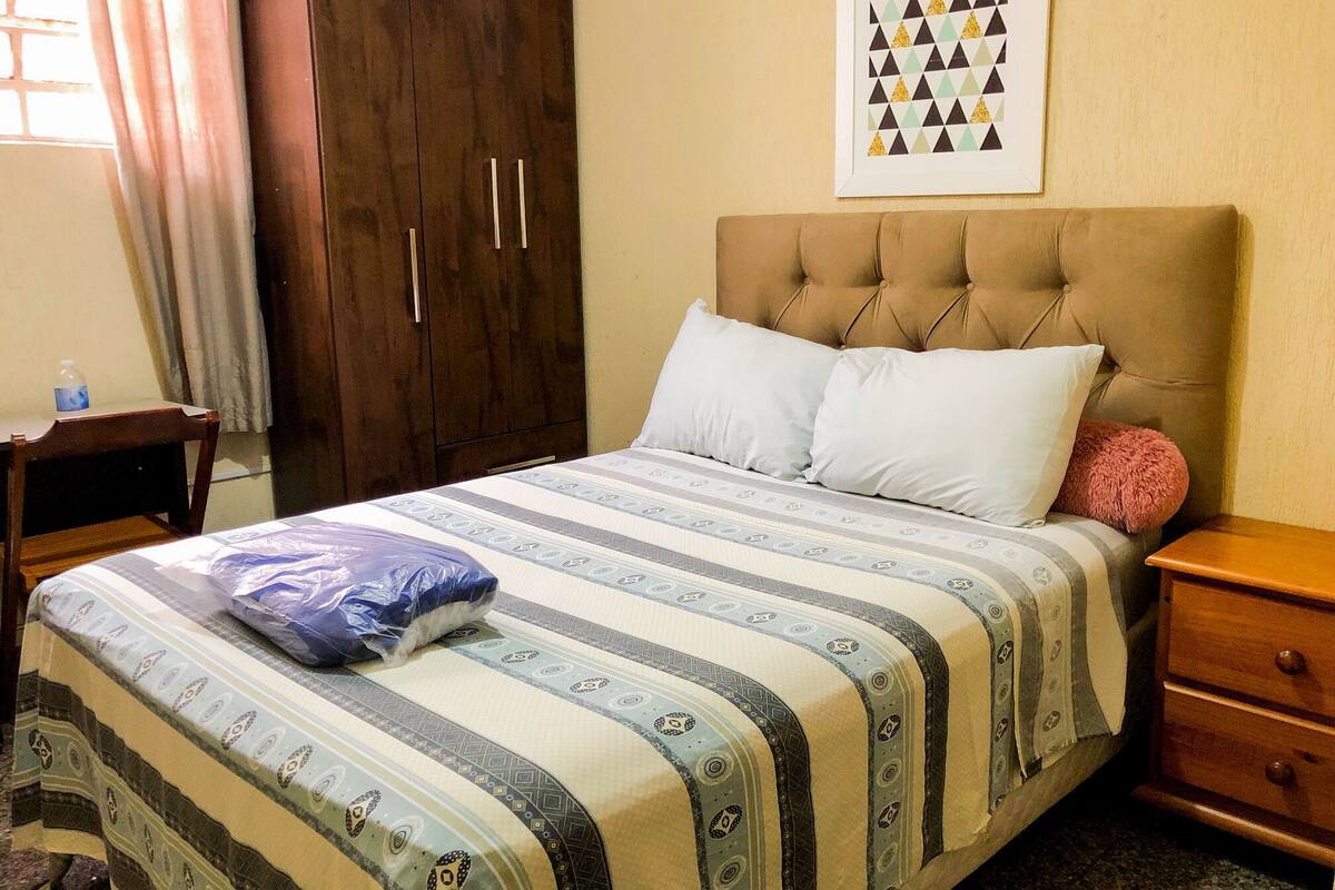 Un dormitorio con cama, un armario de madera, una mesita de noche y un cuadro enmarcado en la pared.