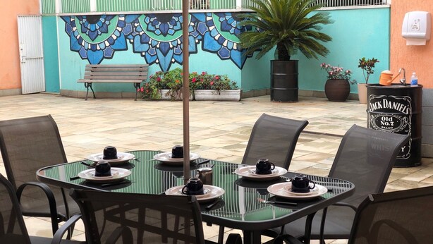 An outdoor seating area with tables and chairs, a mural on the wall, and a potted plant. - Zen Garden Hostel (São Paulo)