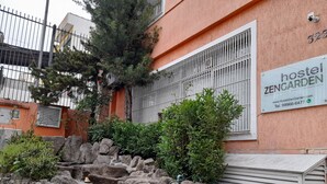 A hostel named 'Zengarden' with a stone wall, greenery, and a metal gate. - Zen Garden Hostel (São Paulo)