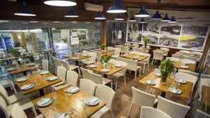 Un restaurant avec de nombreuses tables, des chaises en osier et des suspensions bleues.