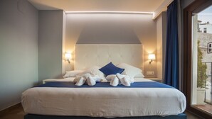 Un lit bien fait, recouvert d’une couvre-lit blanche et bleue, avec deux oreillers et un coussin décoratif bleu. Deux lampes de chevet sont placées de chaque côté du lit.