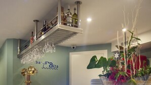 Un comptoir d’accueil avec un plateau blanc à texture, une étagère au-dessus pour y poser des bouteilles et des verres, et une plante en pot ornée de fleurs.