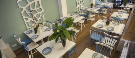 A restaurant with white tables and blue chairs, some with plants on them.