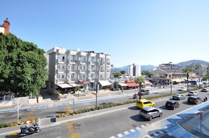 A multi-story building with balconies, a pedestrian area, and a road with vehicles.