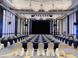 A conference room with rows of tables and chairs, a stage, and a chandelier.