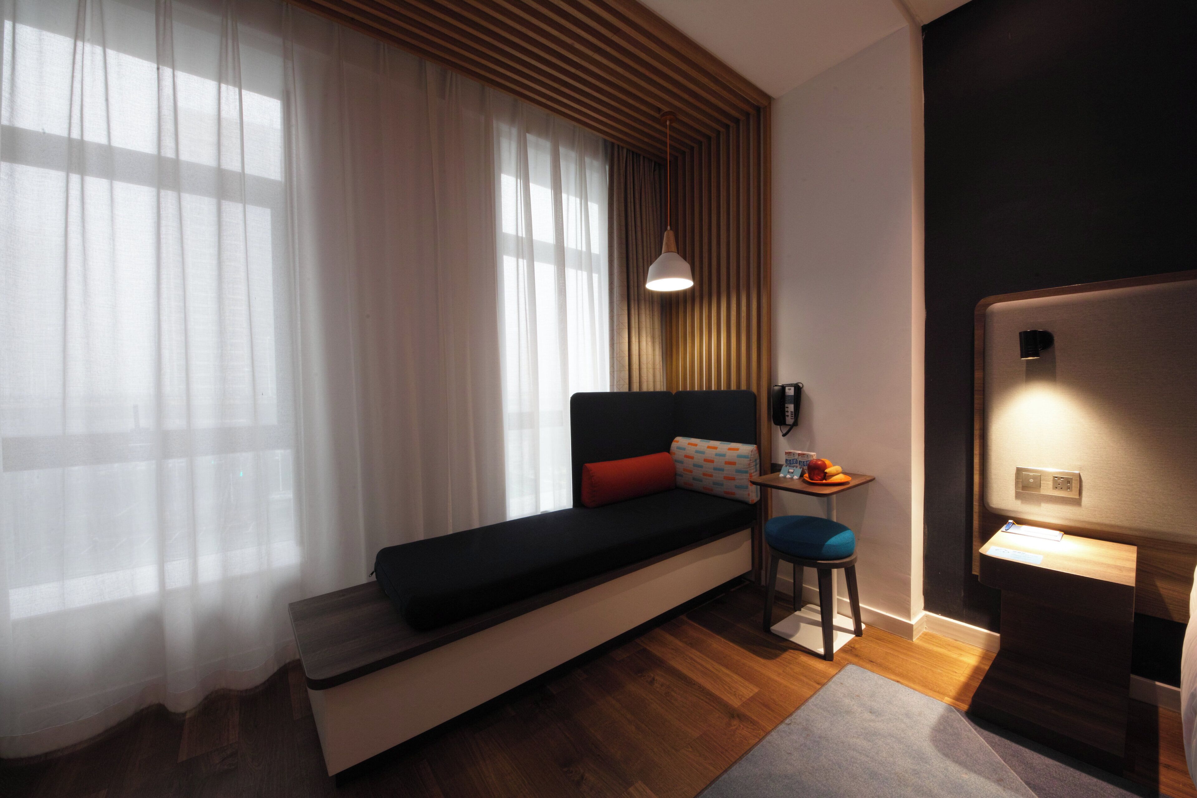 A modern bedroom with a bed, a bedside table, a lamp, and a view of the outdoors.