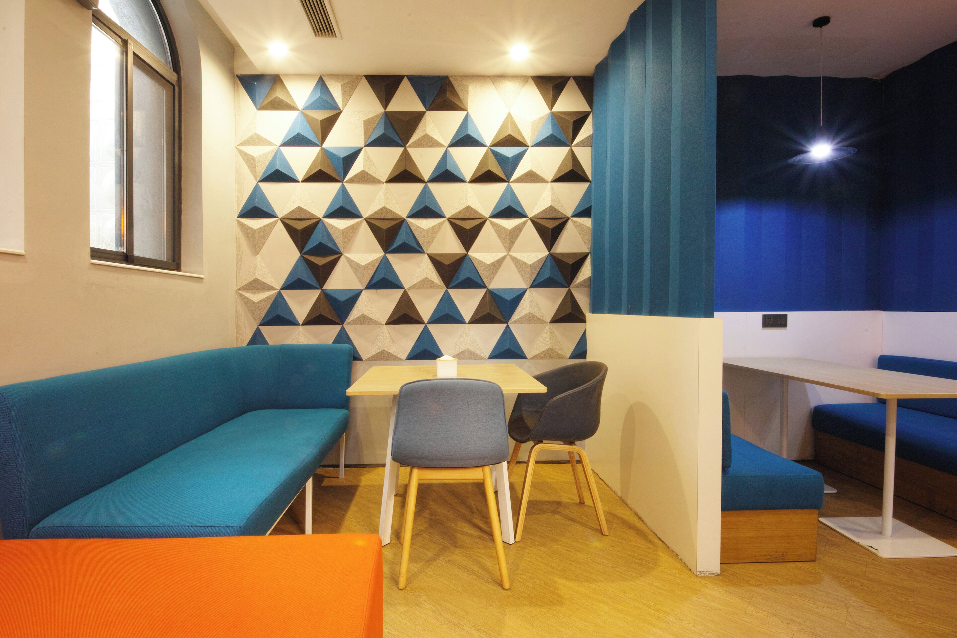 Un intérieur moderne avec un mur orné d’un motif géométrique, un canapé bleu, une table en bois et une petite table à manger avec des chaises.