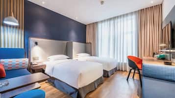 A hotel room with two beds, a desk, a chair, a TV, and a window with curtains.