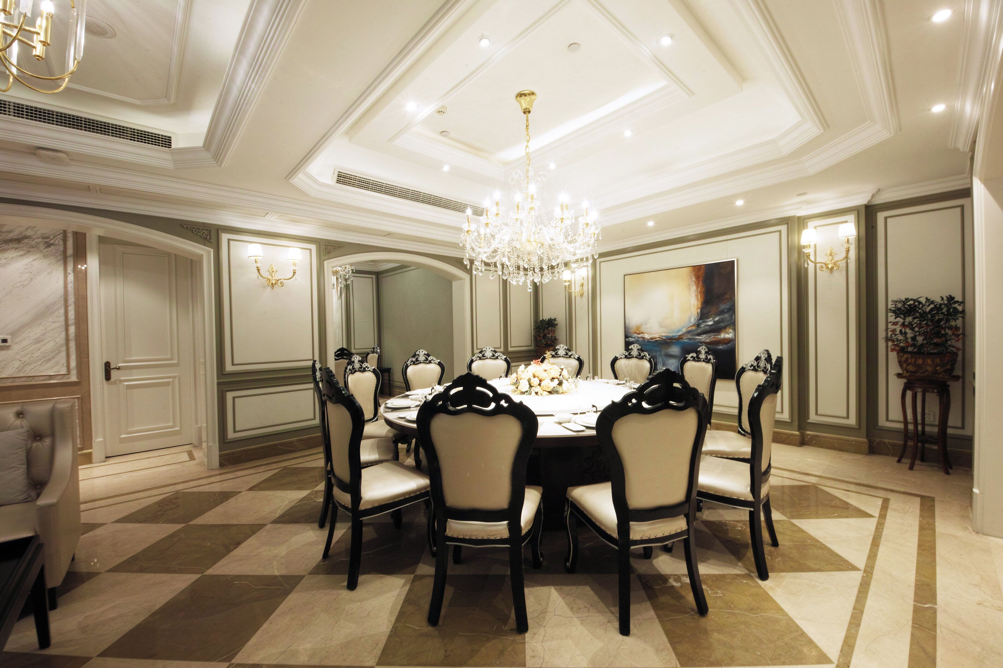 Une salle à manger élégante, avec une grande table ronde, des chaises richement décorées, un lustre et un tableau au mur.
