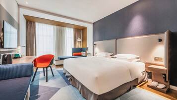 A modern hotel room with a large bed, a desk with a chair, a television, and a window with curtains.