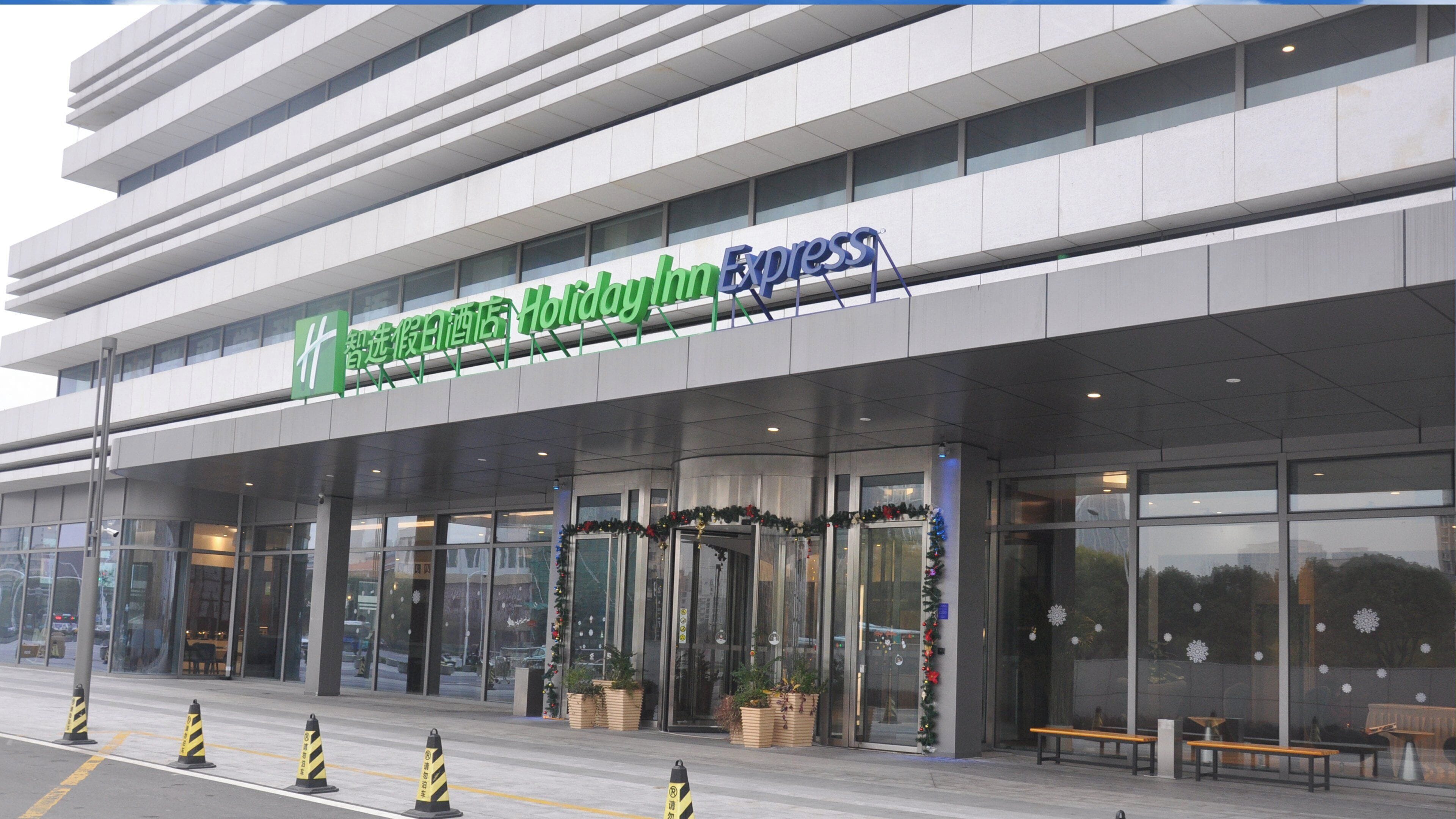 A modern hotel entrance with a large sign, glass doors, and potted plants.