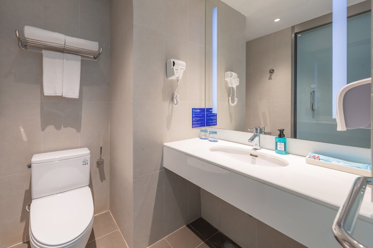 Un baño moderno con inodoro, toallero, secador de manos, secador de pelo y lavamanos con artículos de aseo.