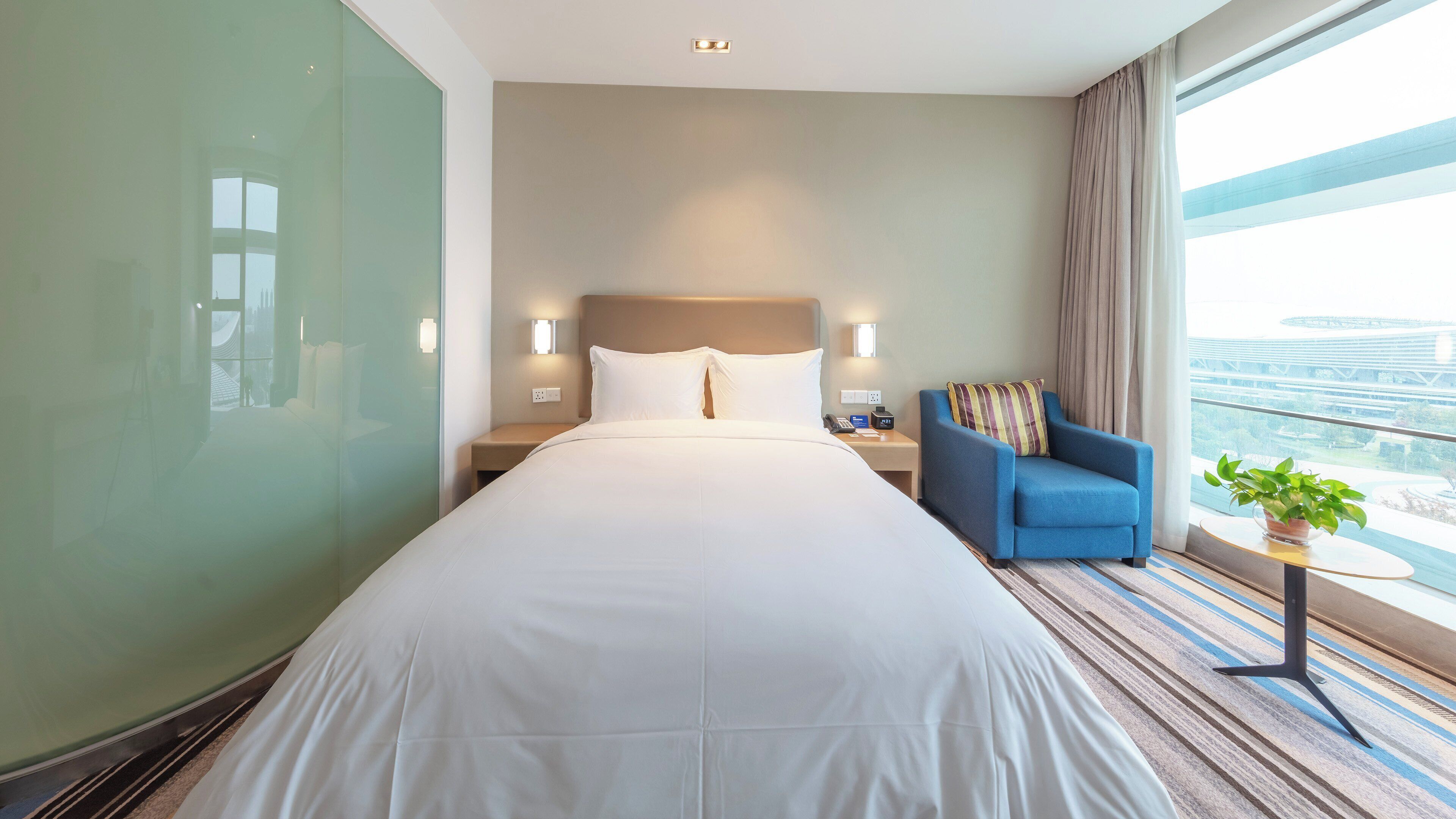 Ein Hotelzimmer mit einem großen Bett, einem blauen Sessel, einem Nachttisch und Blick auf eine Brücke.