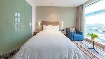 Ein Hotelzimmer mit einem großen Bett, einem blauen Sessel, einem Nachttisch und Blick auf eine Brücke.