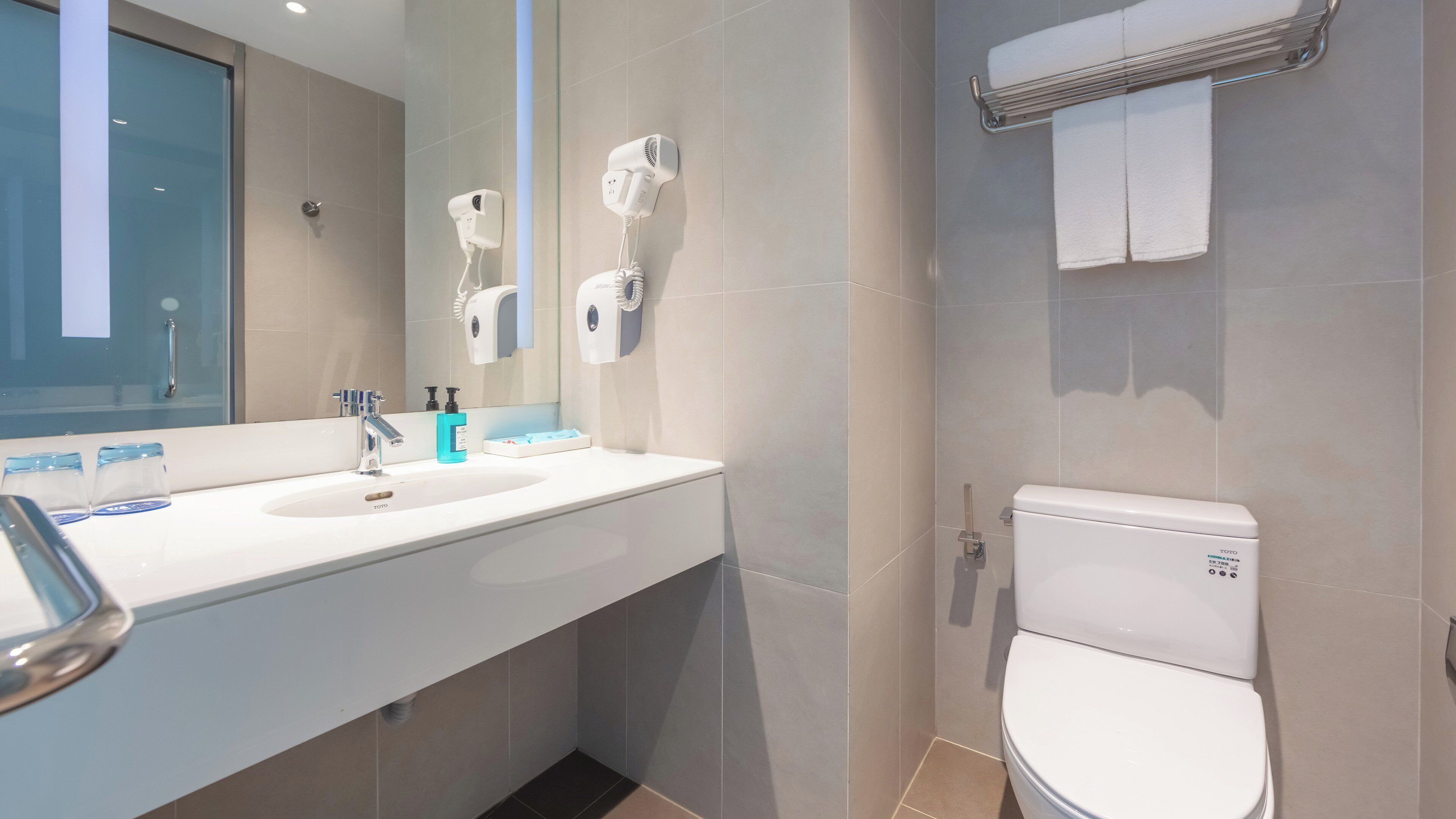 Et moderne badeværelse med vask, spejl, håndtørrer og toilet.