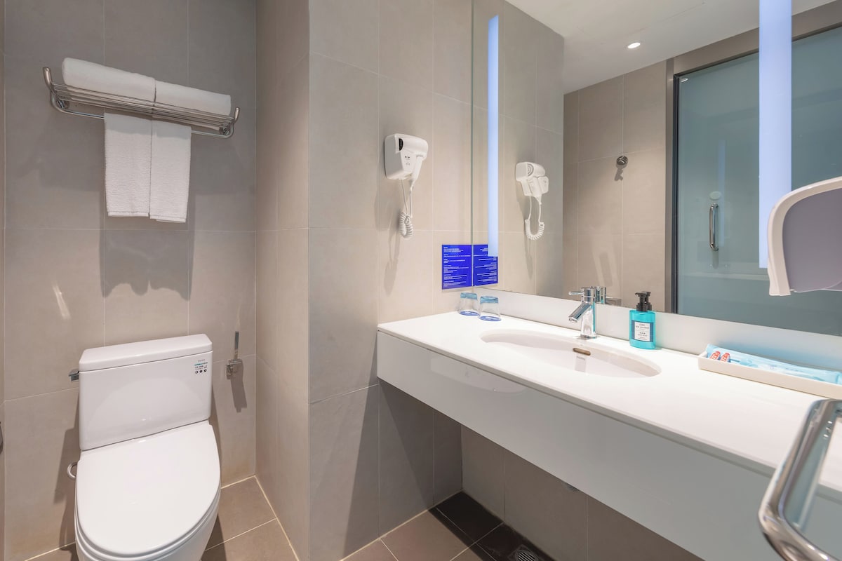 Un baño moderno con inodoro, toallero, secamanos automático, secador de pelo y lavamanos con artículos de aseo.