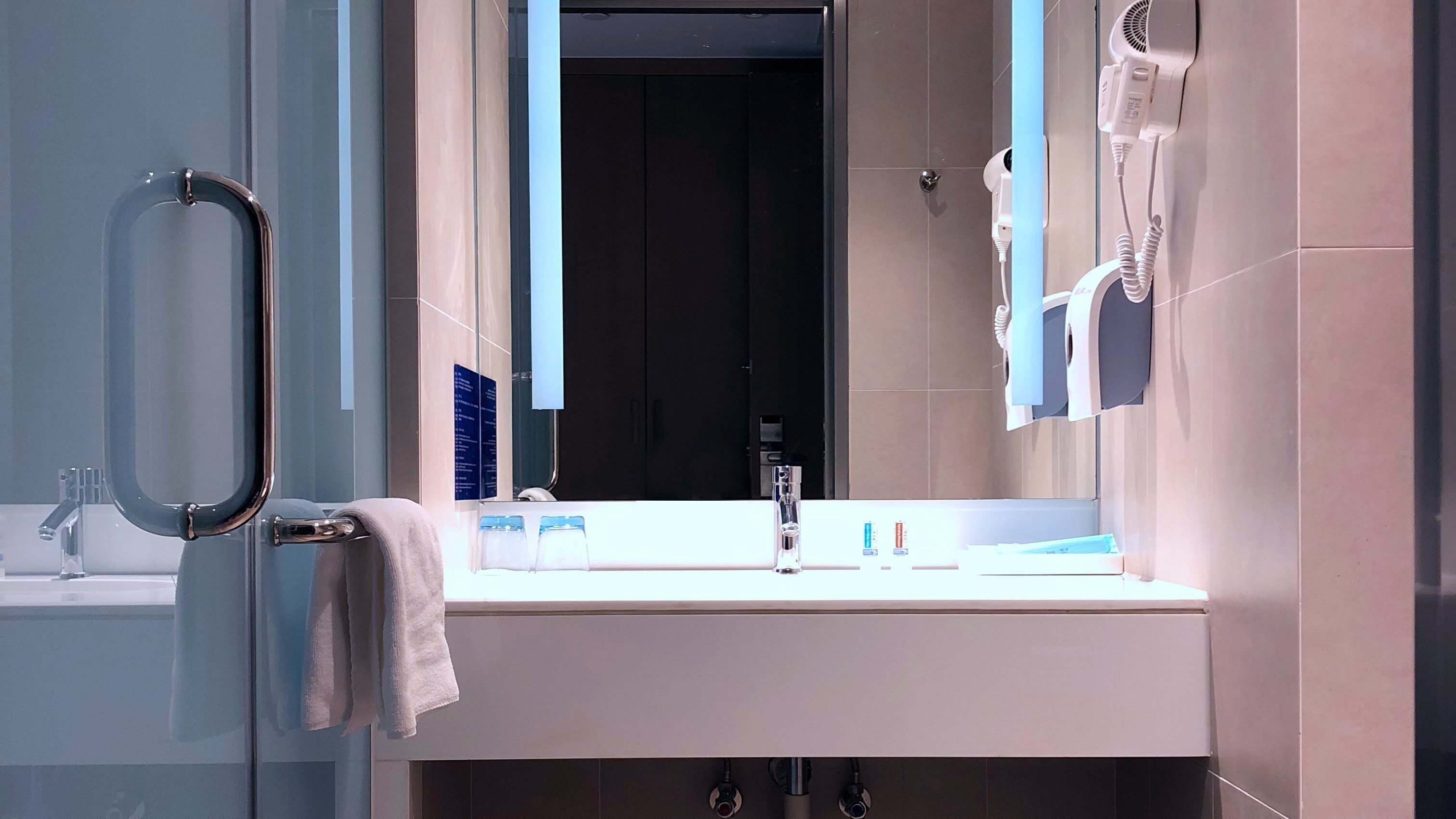 A modern bathroom with a glass door, a white sink, a mirror, and a towel rack.