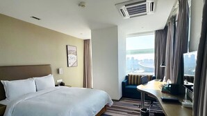 Habitación de hotel con una cama grande, un escritorio con silla, vistas a la ciudad y una ventana con cortinas.