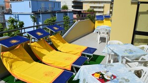 A rooftop terrace with sun loungers, a table with a tray of food, and a view of surrounding buildings. - Hotel Dear (Rimini)