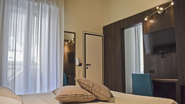 A hotel room with a bed, a TV, a desk, and a door. - Hotel Dear (Rimini)