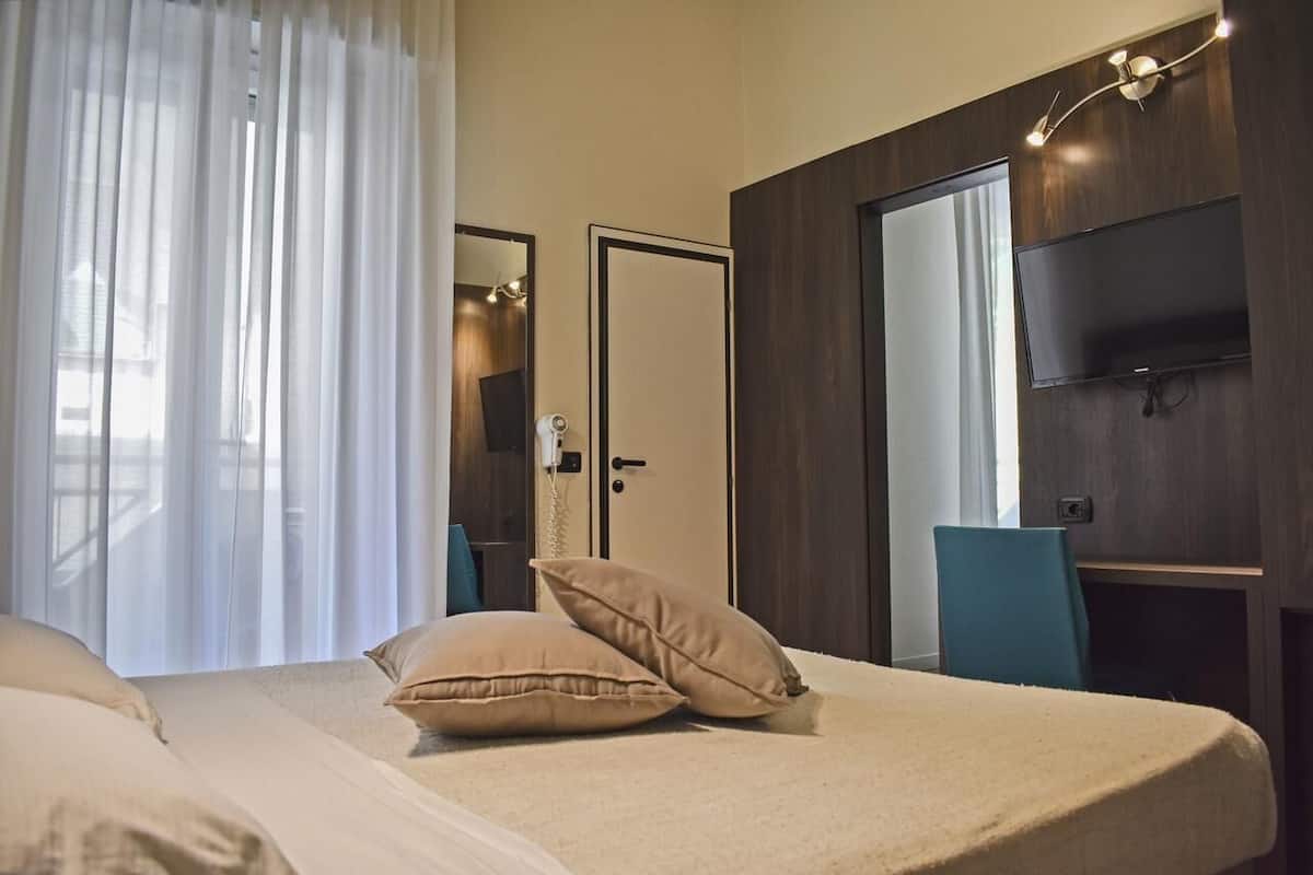 A hotel room with a bed, a TV, a desk, and a door.