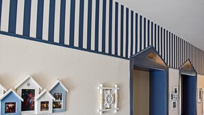 A hallway with a striped wall, a row of small house-shaped photo frames, and a door with a blue frame. - Hotel Dear (Rimini)