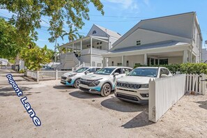 A row of parked cars in front of a building with a covered porch and a white fence. - **GOOD VIBRATIONS @ OLD TOWN** Villa & Pool + Last Key White Glove Service... (Key West)