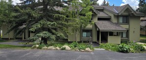 A two-story building with a sloped roof, a front porch, and a large evergreen tree in front.