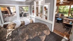 Una habitació àmplia amb una gran roca com a peça central, una zona de seients amb coixins, una prestatgeria i vista a l'exterior.