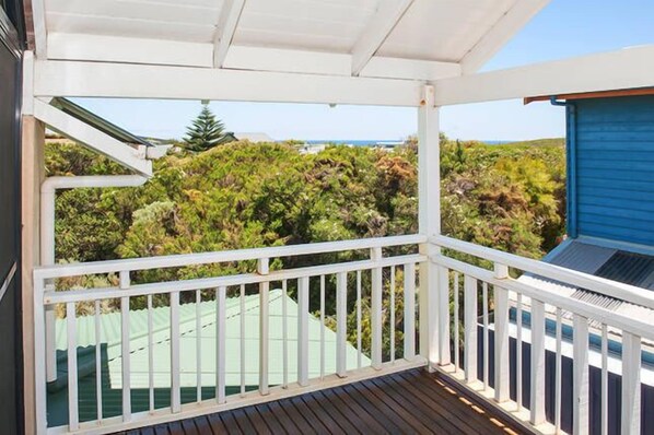 Un espace extérieur abrité, doté d’une terrasse en bois et d’une balustrade blanche, qui offre une vue sur un paysage verdoyant et luxuriant et sur un ciel bleu dégagé.