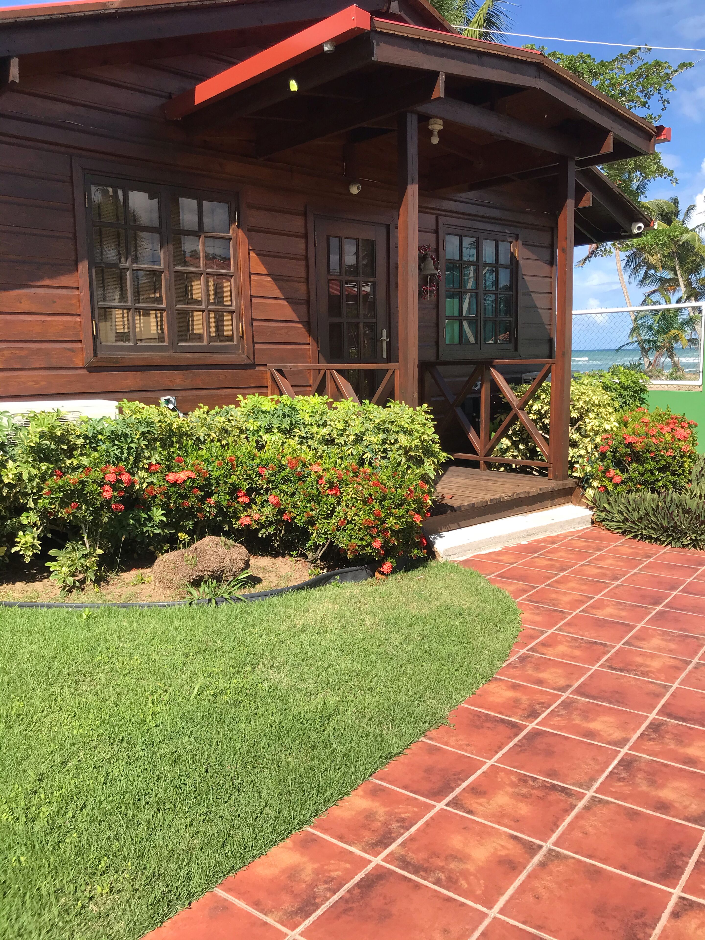 A wooden building with a porch, a well-maintained lawn, and a tiled pathway leading to the entrance.