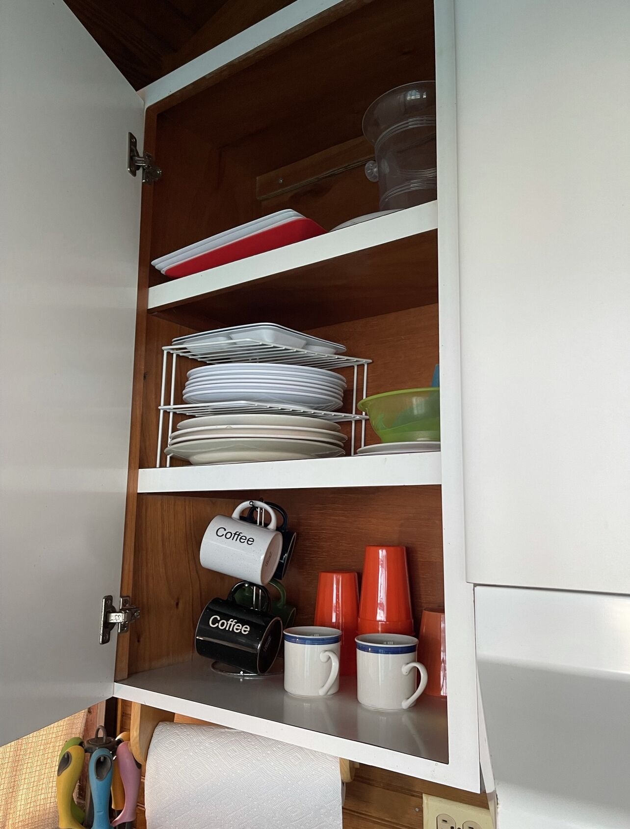 A kitchen cabinet with shelves holding plates, bowls, and coffee mugs.