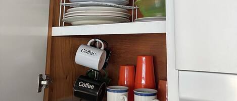 A kitchen cabinet with shelves holding plates, bowls, and coffee mugs.