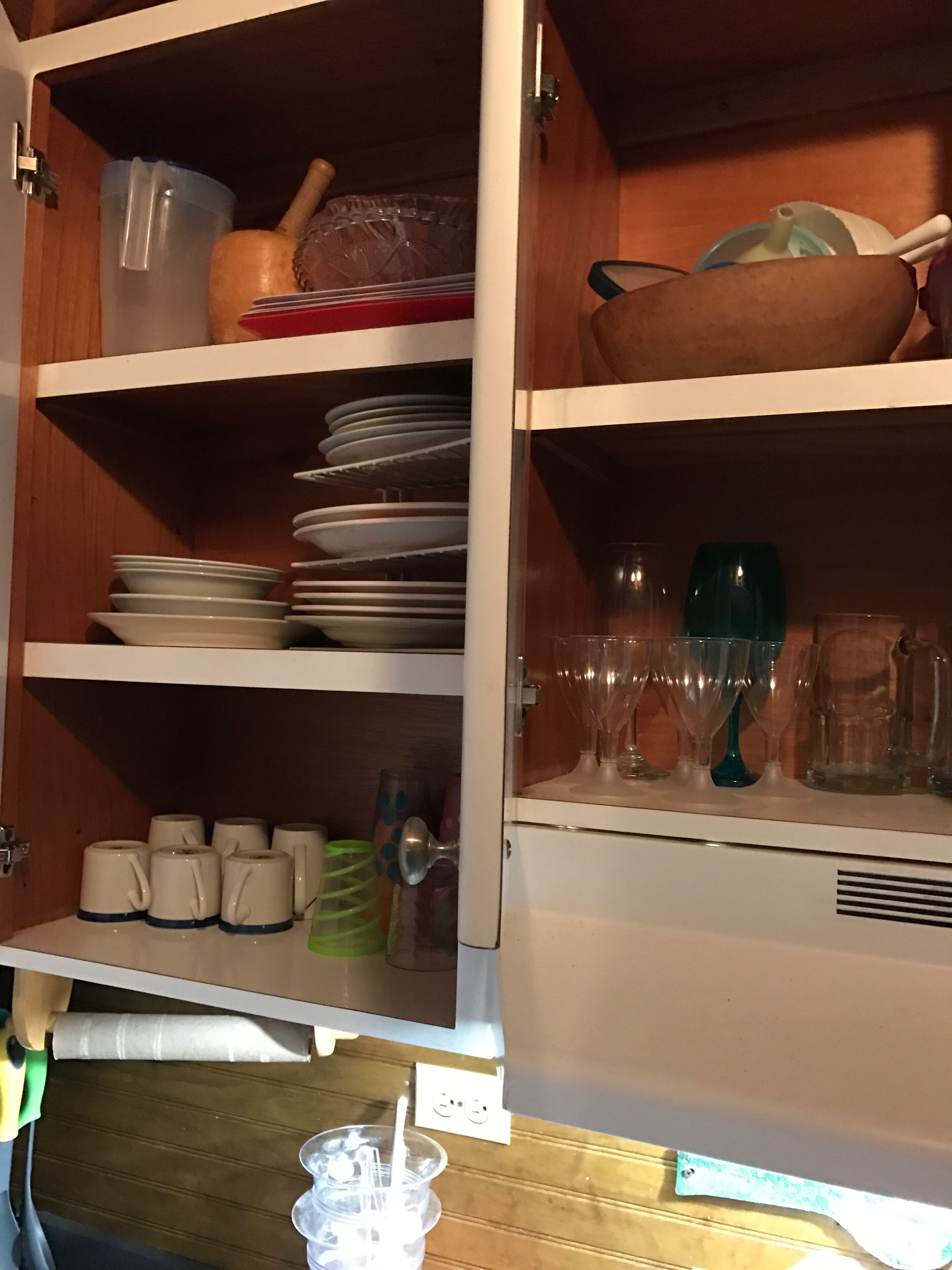 A kitchen cabinet with shelves holding plates, bowls, cups, and glasses.