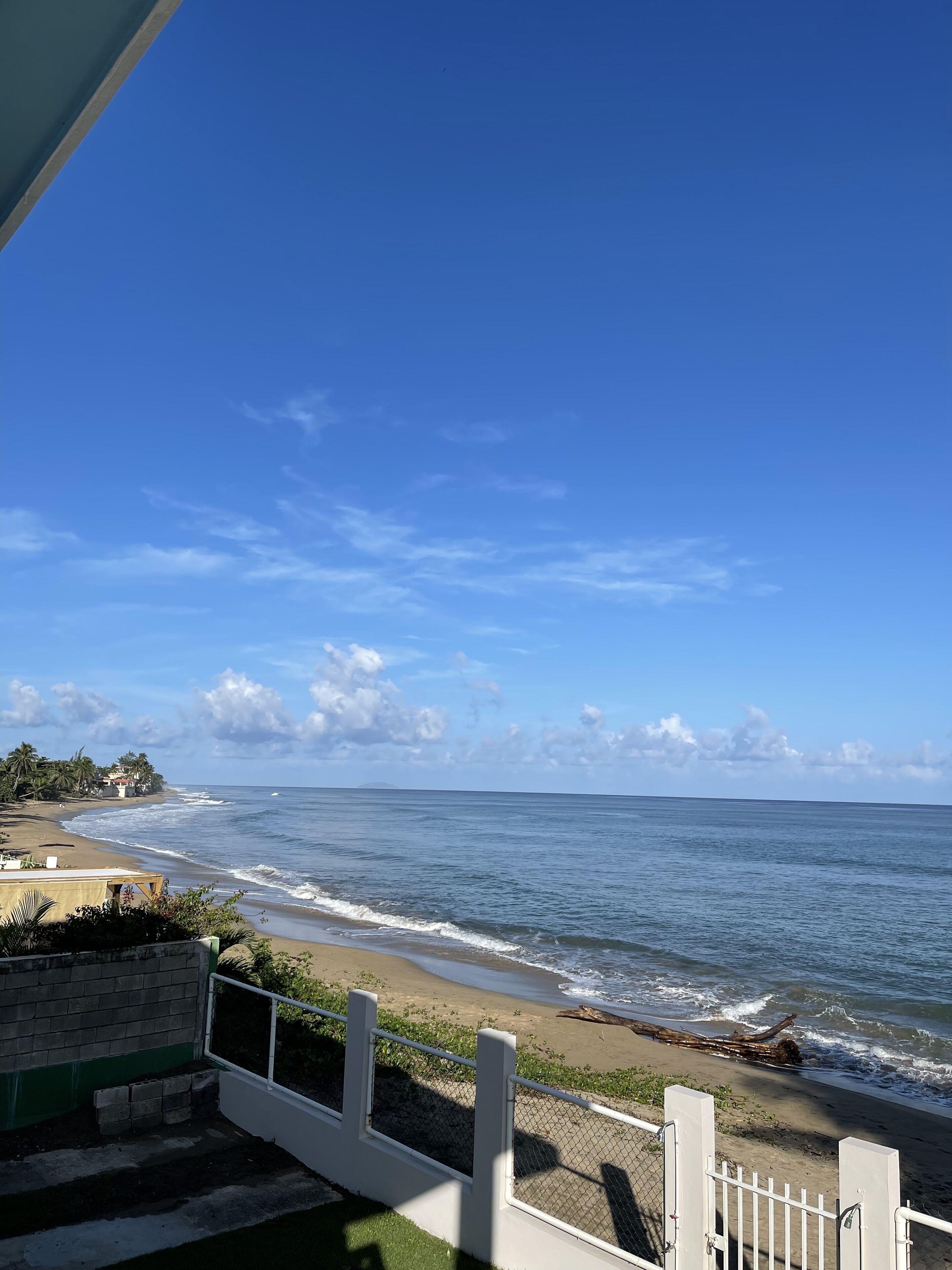 Une vue sur la plage, avec un ciel dégagé, une plage de sable et une clôture au premier plan.