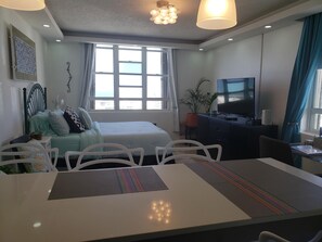 A modern hotel room with a bed, a desk with a computer, a TV, and a large window with curtains. - Apex living in Puerto Rico's capital (Santurce)