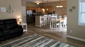 A modern kitchen with wooden cabinets, a stainless steel refrigerator, and a dining area with white chairs and a wooden table.