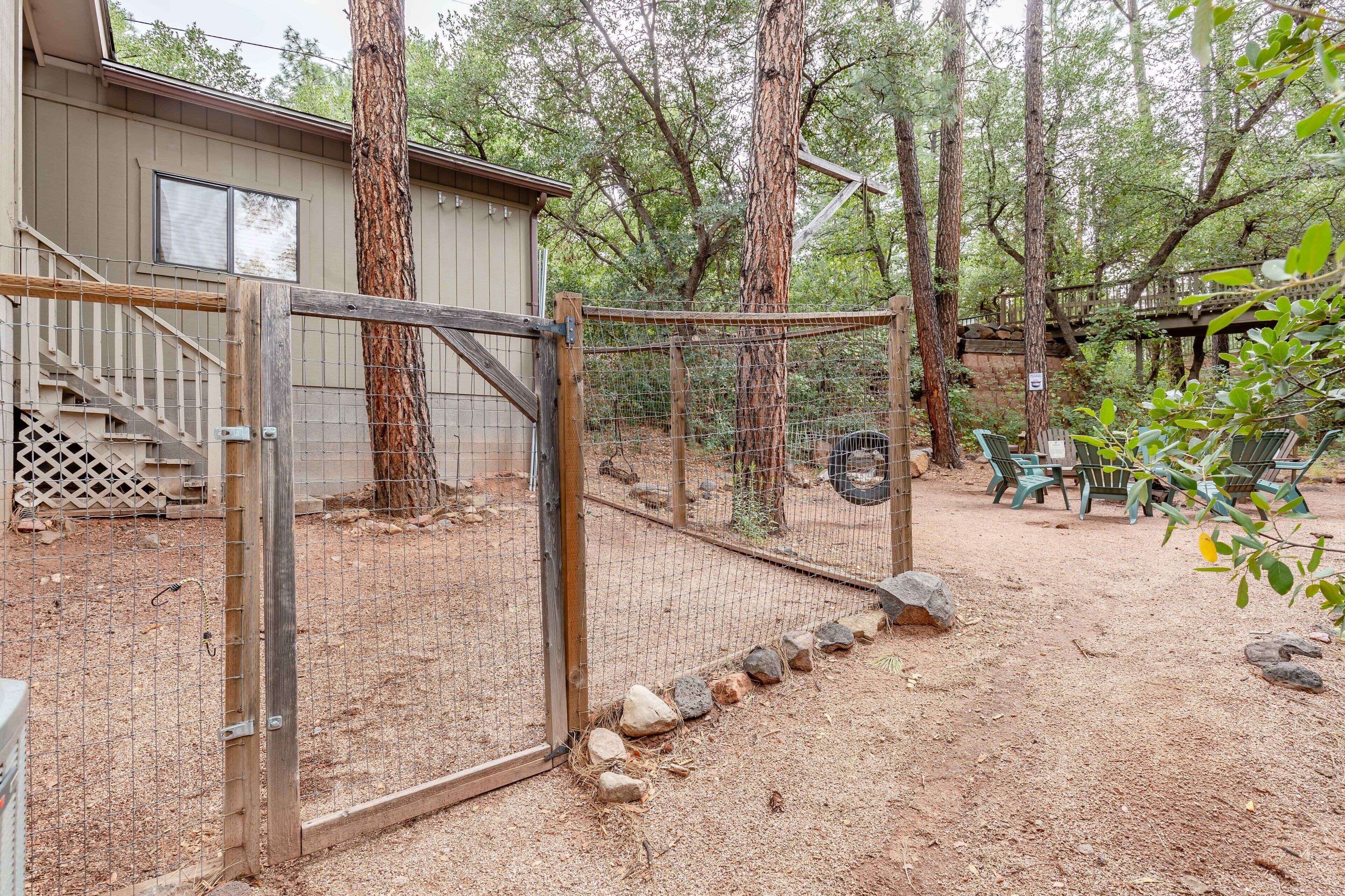 A fenced outdoor area with a wooden gate, a dirt ground, and a building with a window.