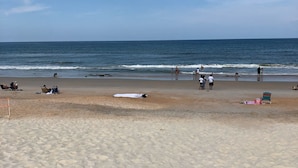 Una spiaggia con cielo sereno, persone che passeggiano sulla riva e sedie a sdraio e ombrelloni.