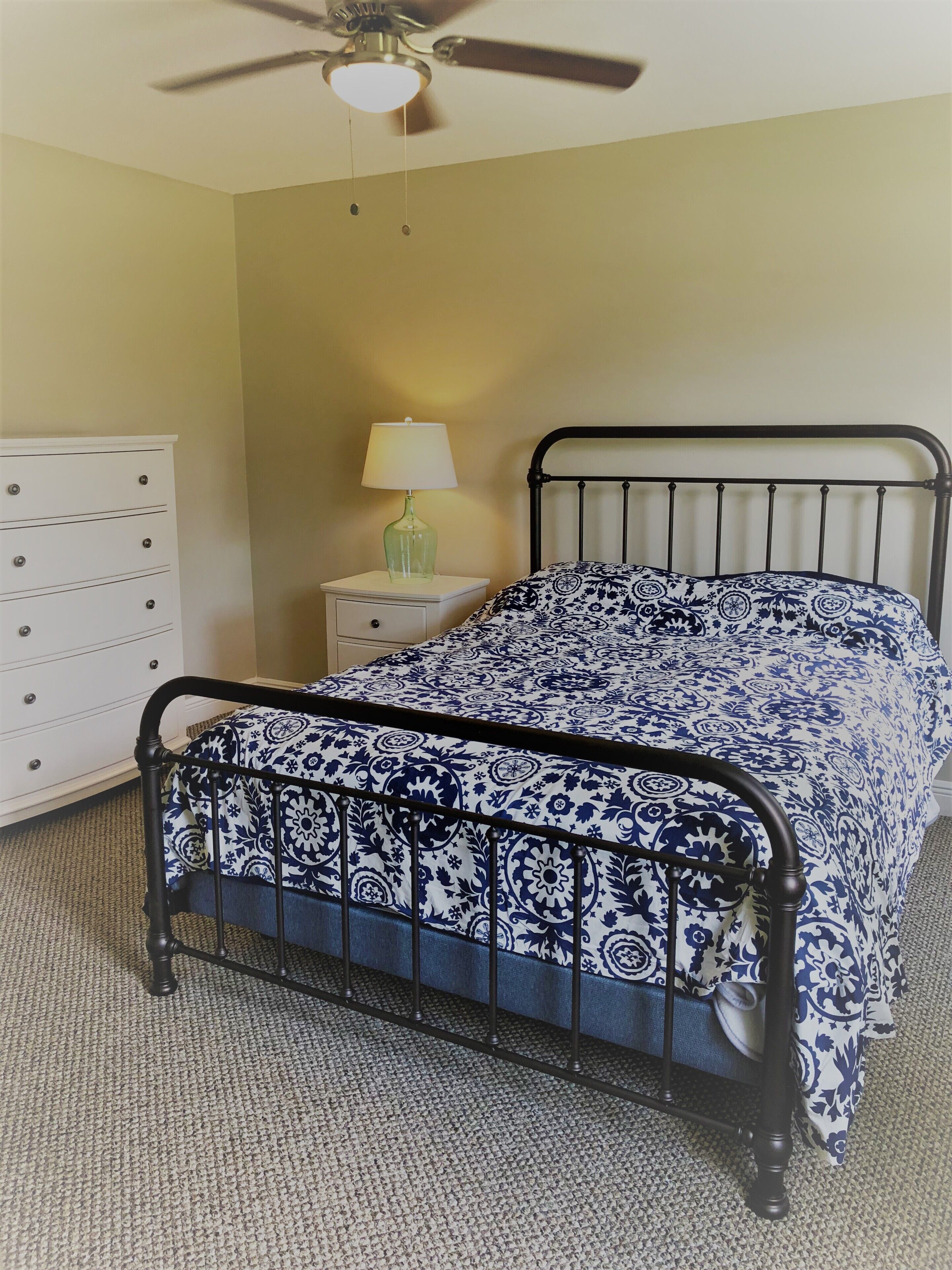 Une chambre à coucher comprenant un lit, une table de chevet, une commode et un ventilateur de plafond.