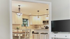 Una cucina moderna con mobili bianchi, un'area pranzo con sedie in legno e una TV a schermo piatto su un supporto bianco.
