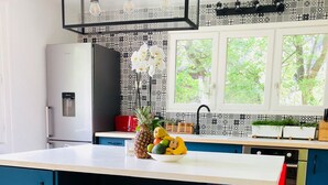 Een moderne keuken met een groot eiland, barstoelen, een koelkast en een raam met uitzicht op groen.