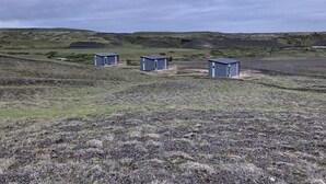 Three small, rectangular buildings in a rural setting with grassy terrain and distant hills. - Afternoon cottages near Hella, Hekla & Landmannalaugar (Hella)