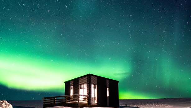 A small wooden cabin with a balcony, surrounded by snow, under a starry night sky with the Northern Lights. - Afternoon cottages near Hella, Hekla & Landmannalaugar (Hella)